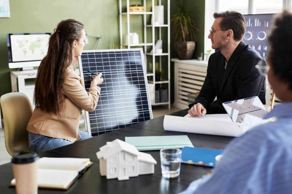 Solarteurin erklaert Ihren Kunden anhand eines PV-Moduls die Funktionsweise von Photovoltaiktechnik in Ihrem Buero